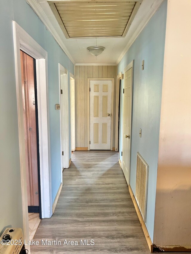 hall with light wood-type flooring, crown molding, baseboards, and visible vents