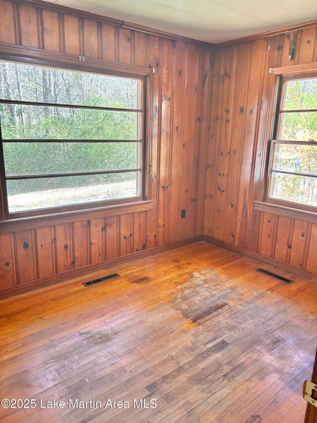empty room featuring wood-type flooring, wood walls, and visible vents