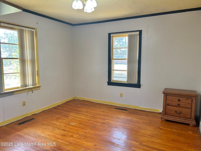 unfurnished room featuring wood finished floors, ornamental molding, and visible vents