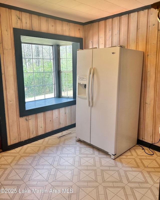 kitchen with white refrigerator with ice dispenser, visible vents, wooden walls, and light floors