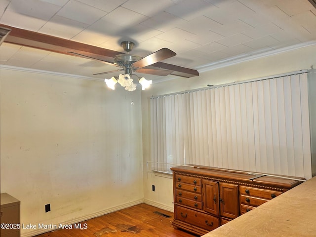 unfurnished bedroom with a ceiling fan, wood finished floors, baseboards, visible vents, and ornamental molding