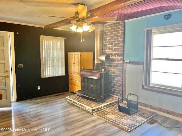 unfurnished living room featuring beam ceiling, a ceiling fan, a wood stove, light wood-style floors, and ornamental molding