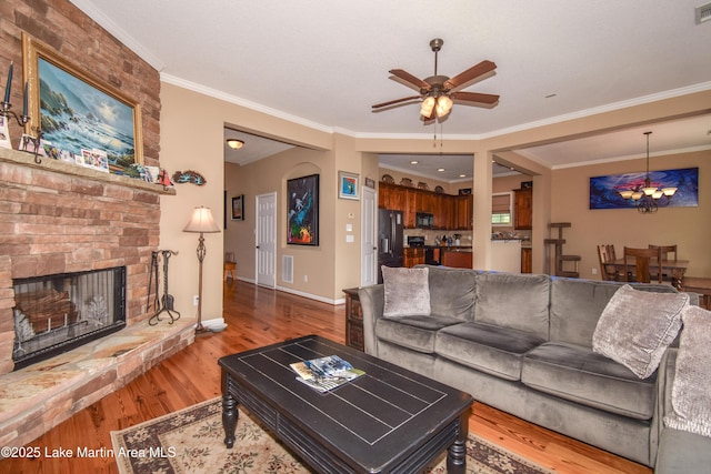 living room featuring hardwood / wood-style flooring, a large fireplace, crown molding, and ceiling fan with notable chandelier