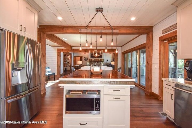 kitchen with stainless steel appliances, wooden walls, a center island, and hanging light fixtures