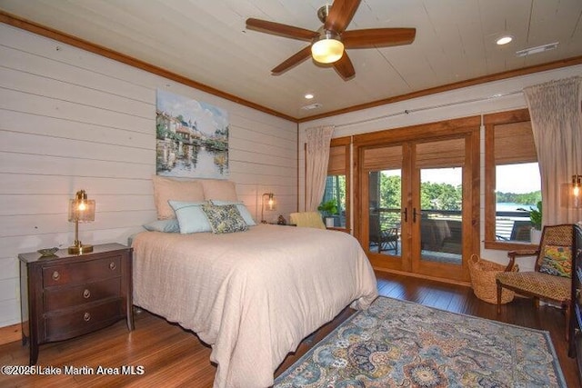 bedroom with crown molding, dark hardwood / wood-style floors, wooden walls, ceiling fan, and access to exterior