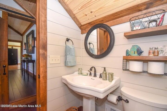 bathroom with lofted ceiling, toilet, sink, wood walls, and wooden ceiling