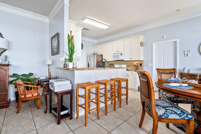 876 Ridge Rd, Dadeville, AL 36853 - kitchen featuring white microwave, stainless steel refrigerator with ice dispenser, ornamental molding, a kitchen bar, and light tile patterned floors
