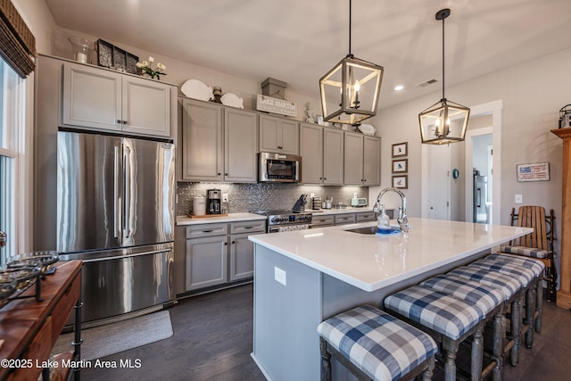 kitchen with gray cabinets, appliances with stainless steel finishes, decorative light fixtures, an island with sink, and sink