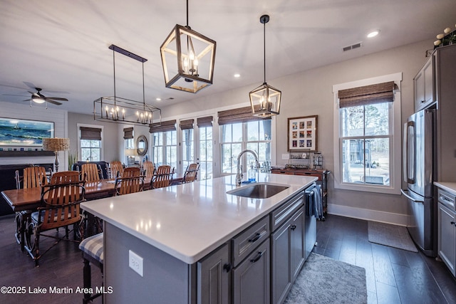 kitchen featuring a kitchen island with sink, sink, hanging light fixtures, and stainless steel refrigerator