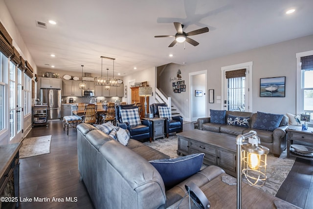 living room with ceiling fan with notable chandelier and dark hardwood / wood-style floors