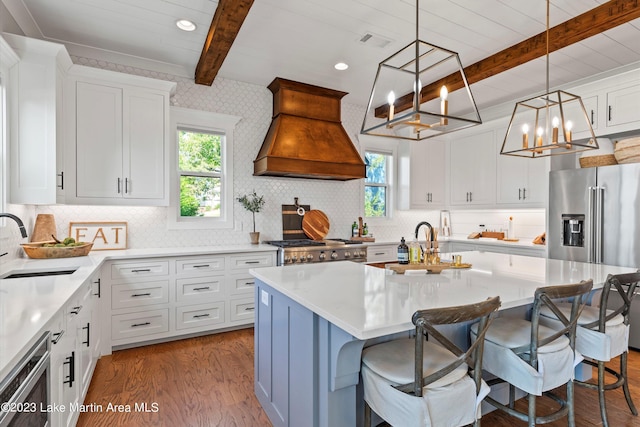 kitchen with custom exhaust hood, a kitchen island with sink, white cabinets, hanging light fixtures, and a breakfast bar area