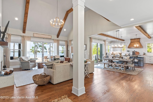 living room with an inviting chandelier, hardwood / wood-style flooring, a towering ceiling, beamed ceiling, and decorative columns