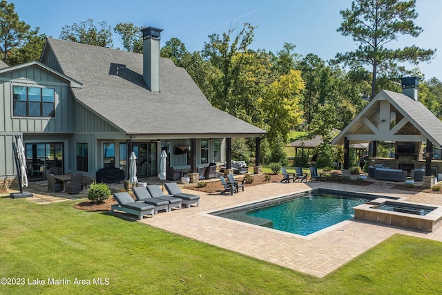 back of property featuring a patio, exterior fireplace, a lawn, and a pool with hot tub