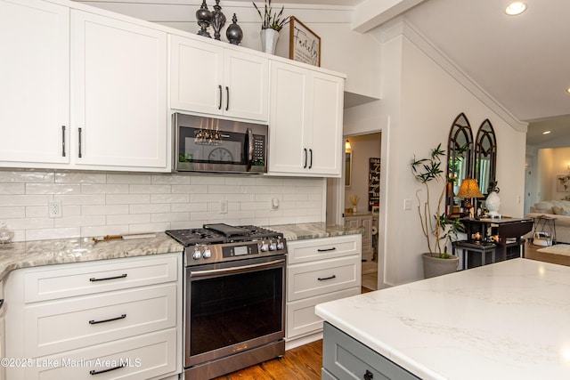 kitchen featuring lofted ceiling, stainless steel appliances, tasteful backsplash, light stone counters, and white cabinets