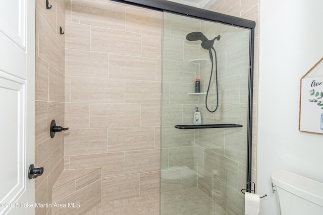 bathroom featuring a shower with door and toilet