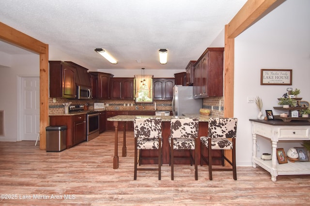 93 Restful Cv, Dadeville, AL 36853 - kitchen featuring appliances with stainless steel finishes, a peninsula, light wood finished floors, tasteful backsplash, and a breakfast bar area