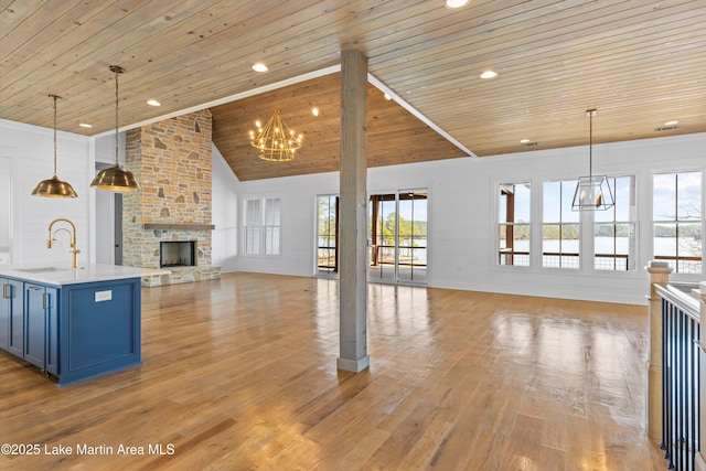 unfurnished living room with a notable chandelier, light wood-style flooring, a sink, a stone fireplace, and wooden ceiling