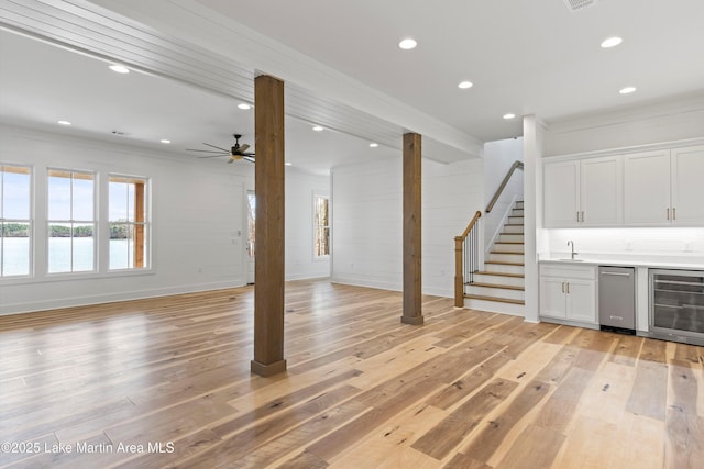 unfurnished living room featuring stairway, wine cooler, light wood-style flooring, and a wealth of natural light