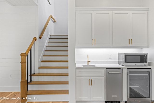 stairs featuring wine cooler, hardwood / wood-style floors, and wet bar