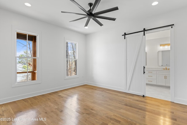 unfurnished bedroom with a barn door, light wood-style flooring, recessed lighting, and baseboards