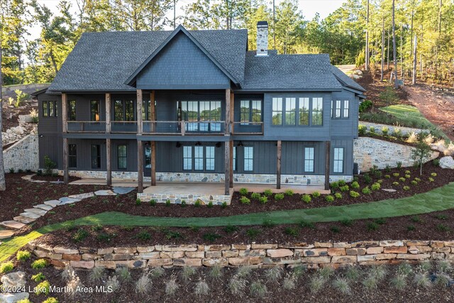 back of house featuring board and batten siding, a chimney, a patio, and roof with shingles