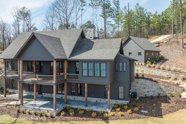 rear view of house with a patio area, board and batten siding, a chimney, and roof with shingles