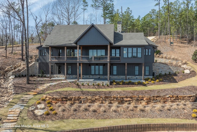 rear view of property with a balcony, a shingled roof, a chimney, and a patio area