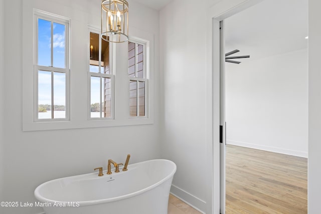 bathroom featuring a notable chandelier, baseboards, a freestanding bath, and wood finished floors