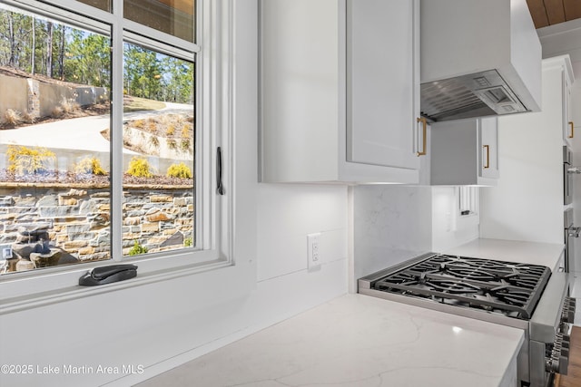 kitchen featuring stainless steel gas range oven, custom range hood, light stone counters, decorative backsplash, and white cabinetry