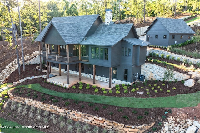 back of house with central air condition unit, a chimney, a patio, and roof with shingles