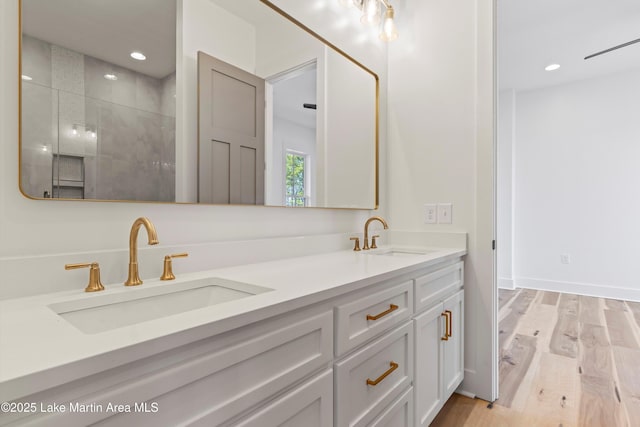 full bathroom featuring a sink, tiled shower, wood finished floors, and double vanity