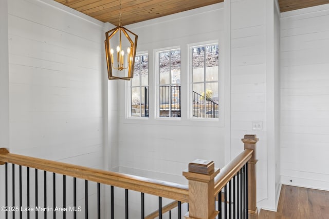 hallway featuring wooden walls, wood finished floors, wooden ceiling, an upstairs landing, and a chandelier