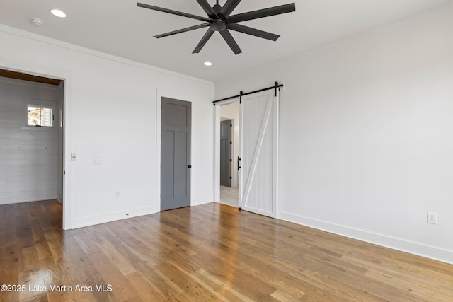 unfurnished bedroom featuring wood finished floors, baseboards, recessed lighting, crown molding, and a barn door