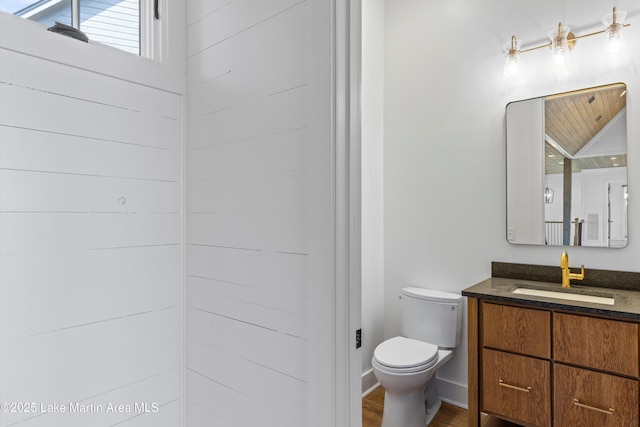 bathroom with vanity, toilet, wood finished floors, and baseboards