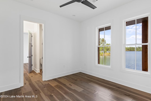 empty room with ceiling fan, a water view, and dark wood-type flooring