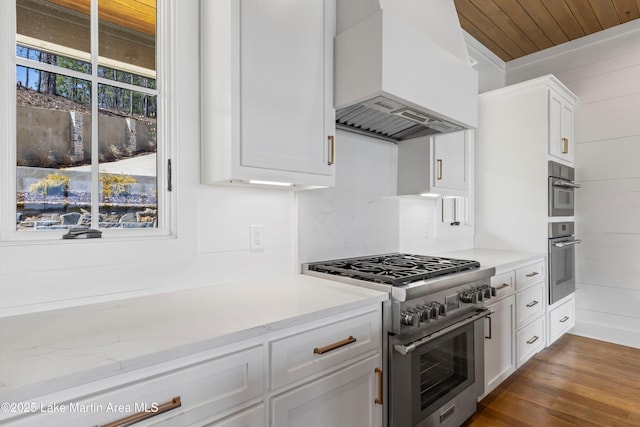 kitchen with light stone countertops, dark wood finished floors, stainless steel appliances, custom range hood, and white cabinetry