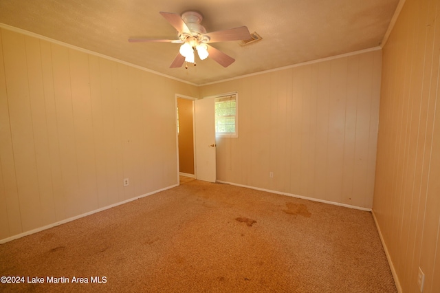 spare room with carpet, ceiling fan, crown molding, and wood walls