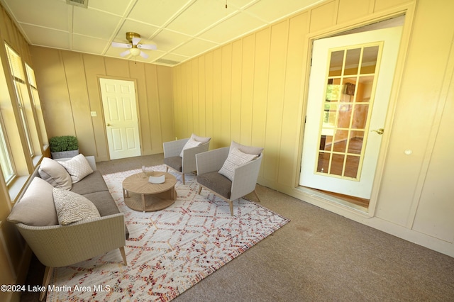 living area with carpet flooring, ceiling fan, and wooden walls