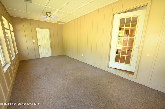 unfurnished room with carpet floors, ceiling fan, and wood walls