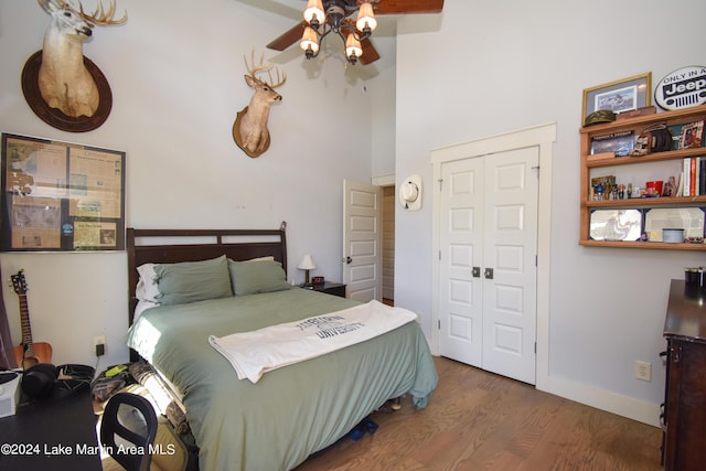 bedroom with ceiling fan, a closet, a towering ceiling, and wood-type flooring