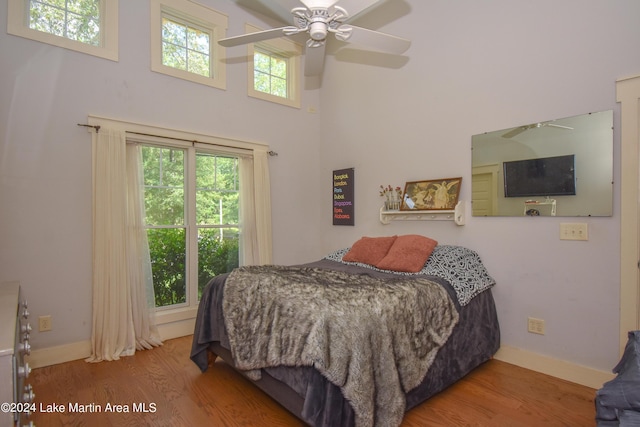 bedroom featuring a towering ceiling, hardwood / wood-style flooring, multiple windows, and ceiling fan