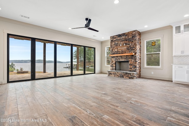 unfurnished living room with a fireplace, a water view, ornamental molding, light hardwood / wood-style flooring, and ceiling fan