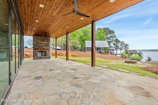 view of patio featuring ceiling fan, a water view, and an outdoor stone fireplace