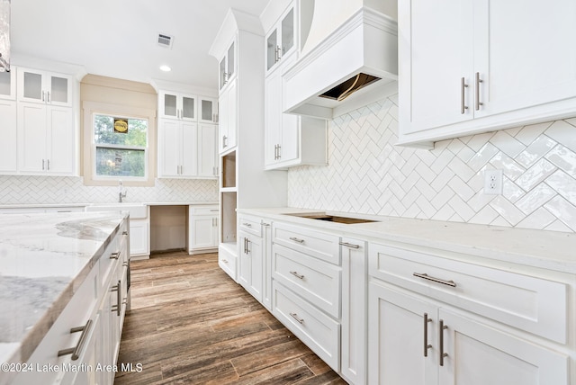 kitchen with light stone countertops, premium range hood, decorative backsplash, white cabinets, and dark wood-type flooring