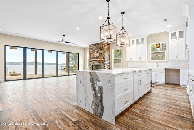 kitchen with decorative backsplash, white cabinets, a kitchen island, a water view, and light stone counters