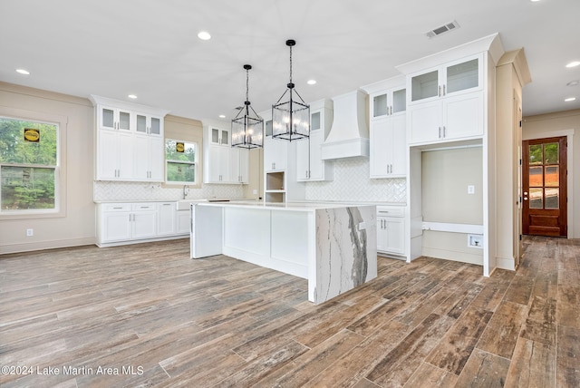 kitchen featuring premium range hood, a center island, white cabinets, and pendant lighting