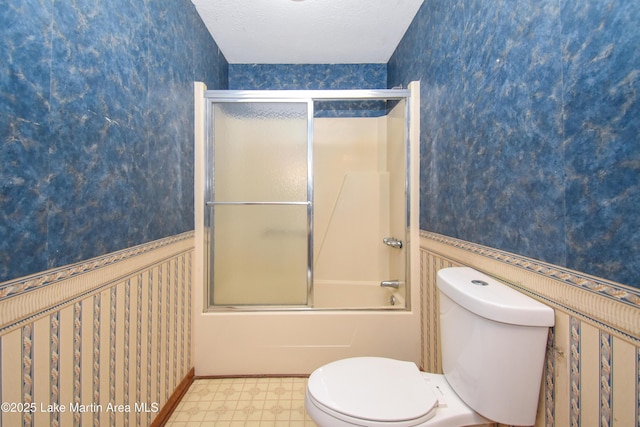 bathroom featuring a textured ceiling, toilet, and bath / shower combo with glass door