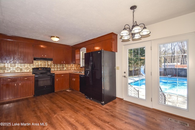 kitchen featuring an inviting chandelier, tasteful backsplash, dark hardwood / wood-style floors, decorative light fixtures, and black appliances