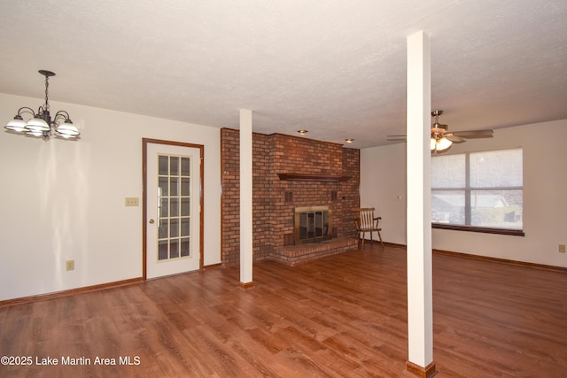 unfurnished living room featuring hardwood / wood-style flooring, ceiling fan with notable chandelier, a textured ceiling, and a brick fireplace