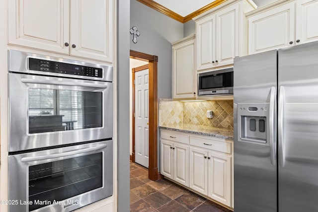 kitchen with decorative backsplash, stone finish floor, appliances with stainless steel finishes, light stone counters, and cream cabinets